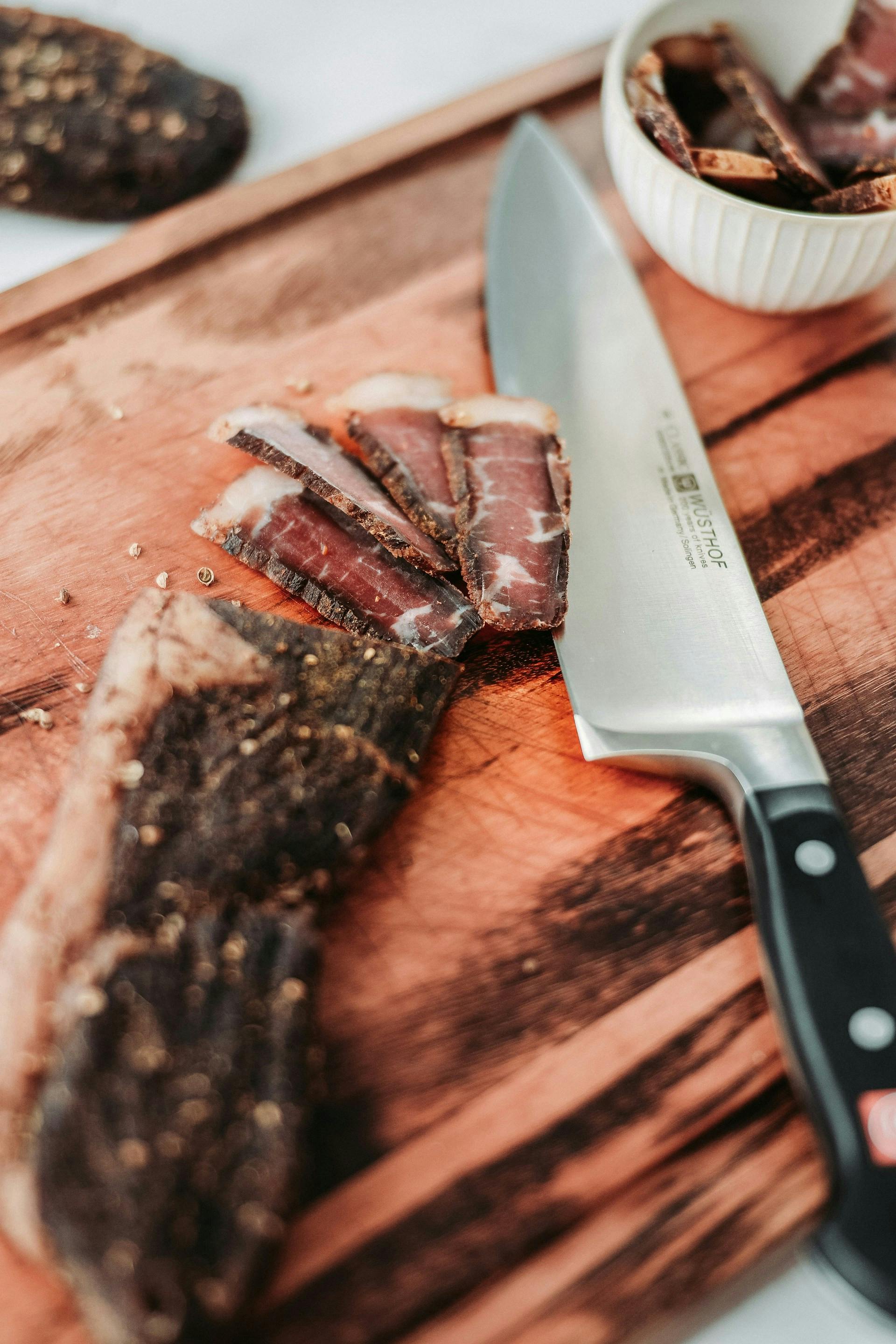 Scharfes Küchenmesser und feingeschnittenes Fleisch liegen auf einem Holzbrett