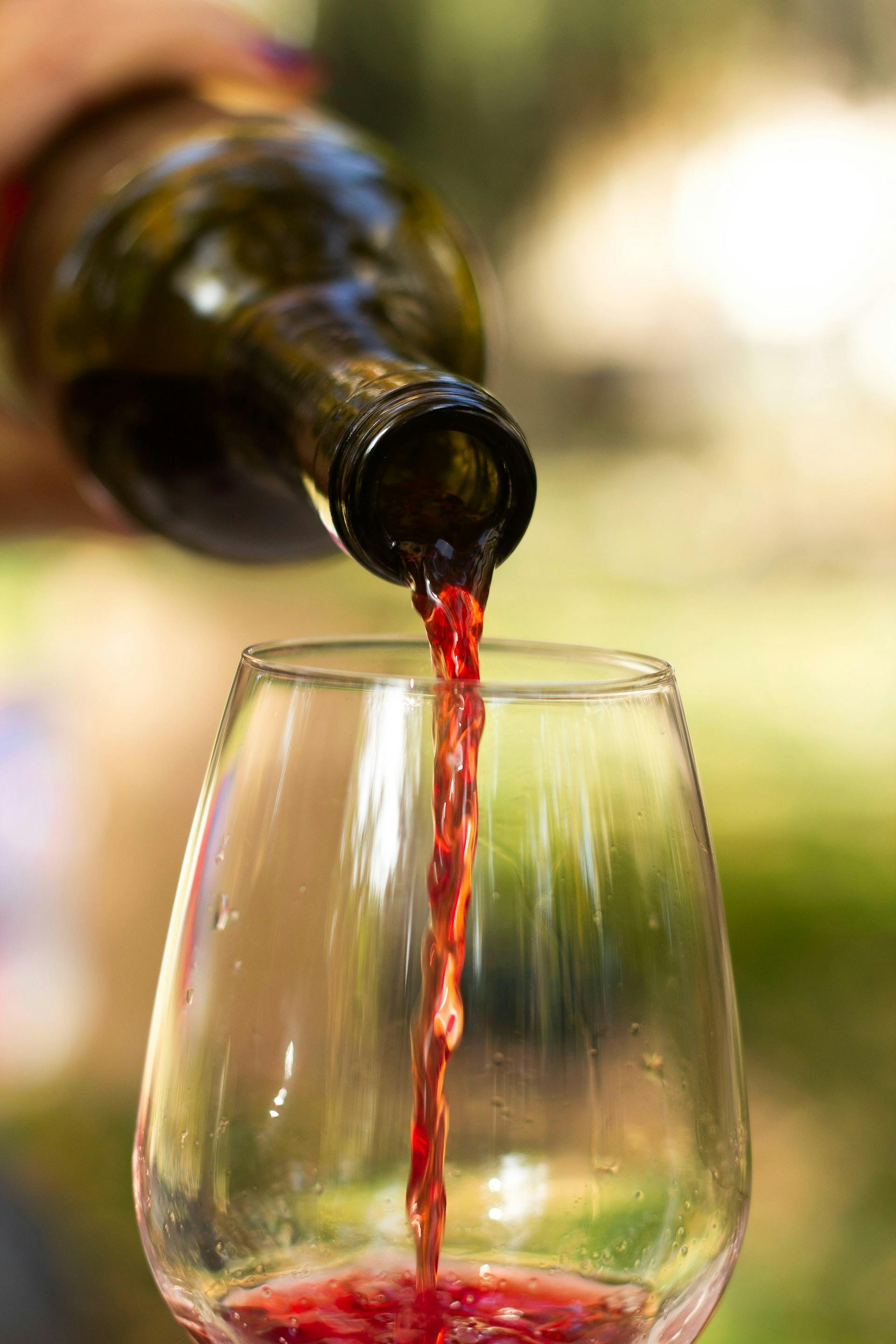 In Weinglas wird rote Flüssigkeit aus Weinflasche eingefüllt