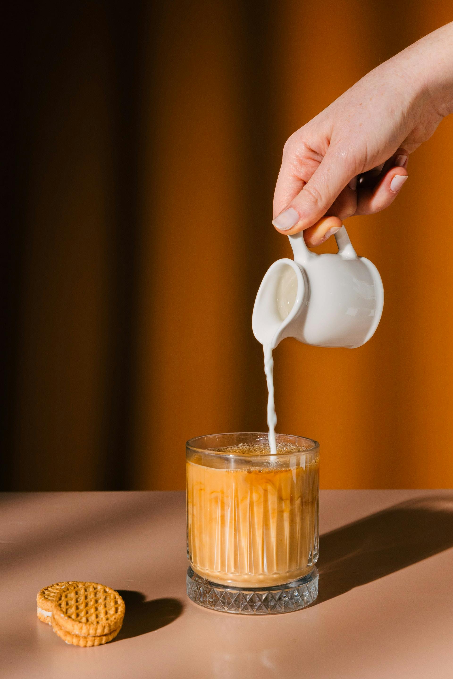 Kaffee in Glas wird mit Milch gefüllt