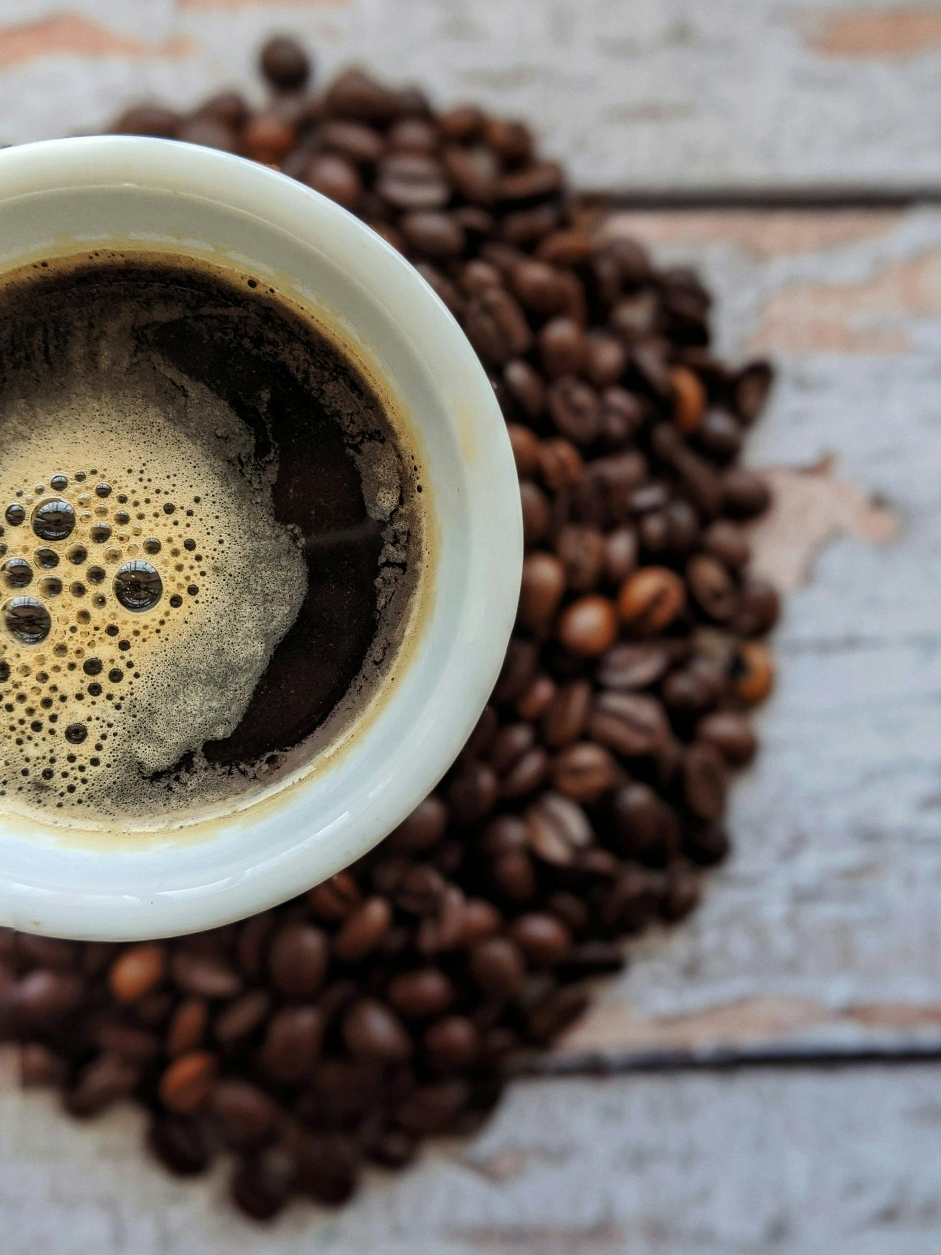 Kaffeetasse mit brauner Flüssigkeit drinnen und drumherum braune Kaffeebohnen