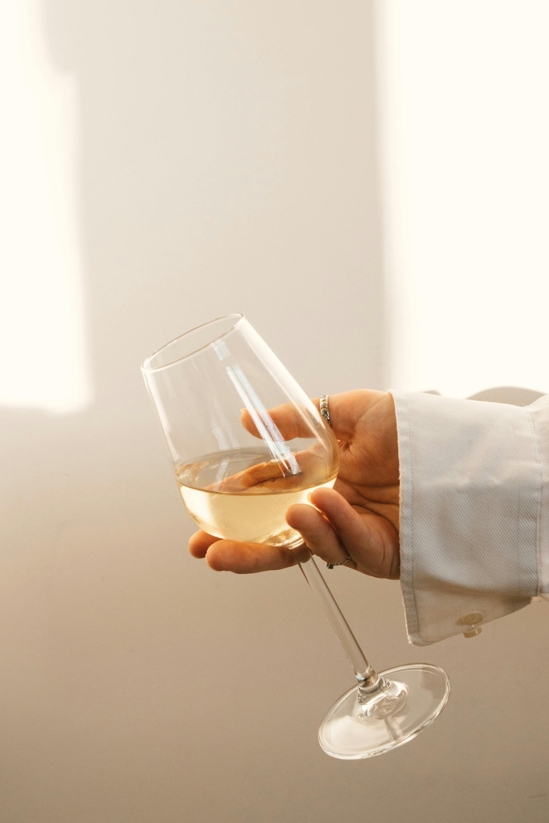 Person hält Weinglas mit klarer Flüssigkeit vor Wand 
