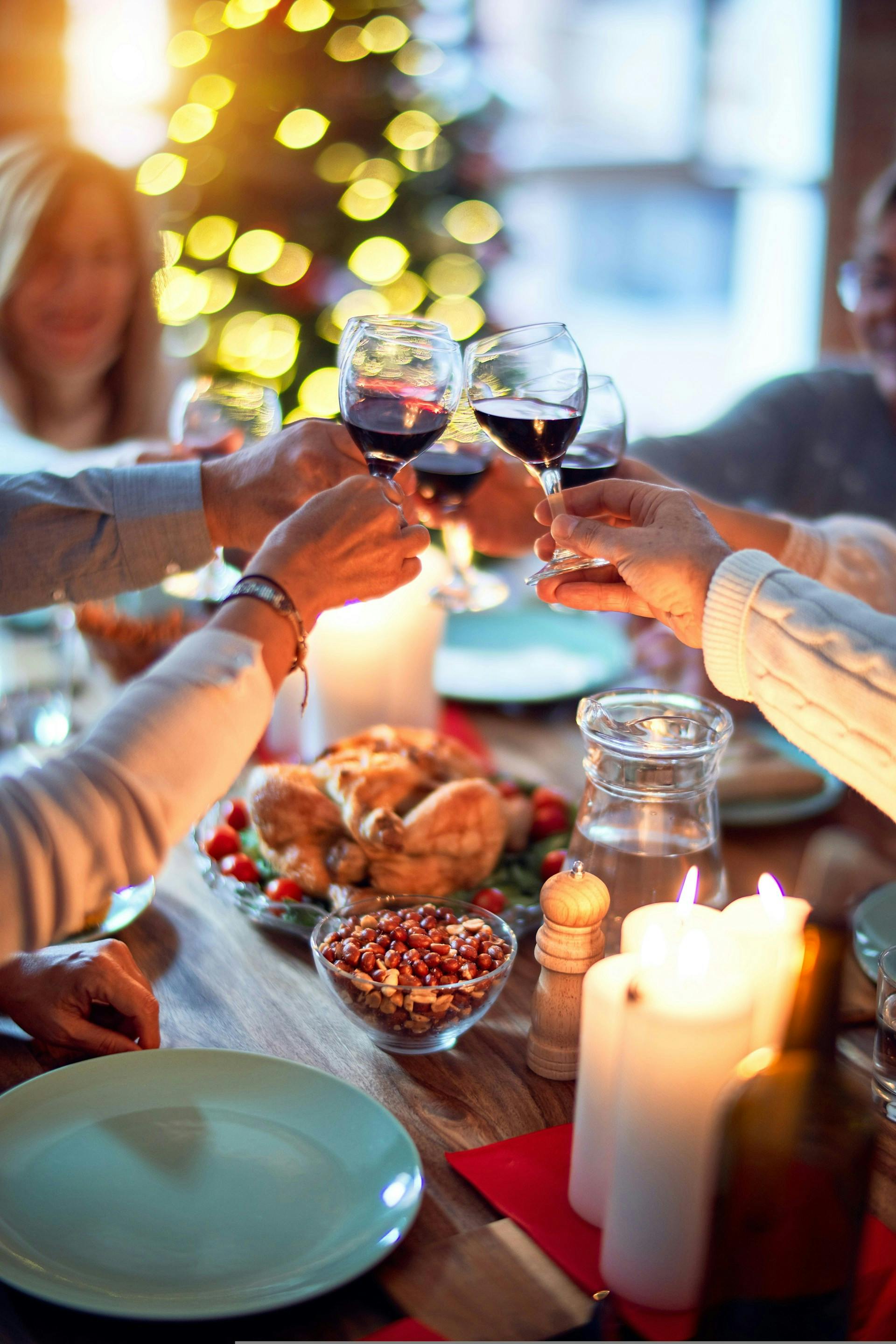 Viele Menschen stoßen mit Gläsern an über den gedeckten Tisch, mit Essen und Kerzen