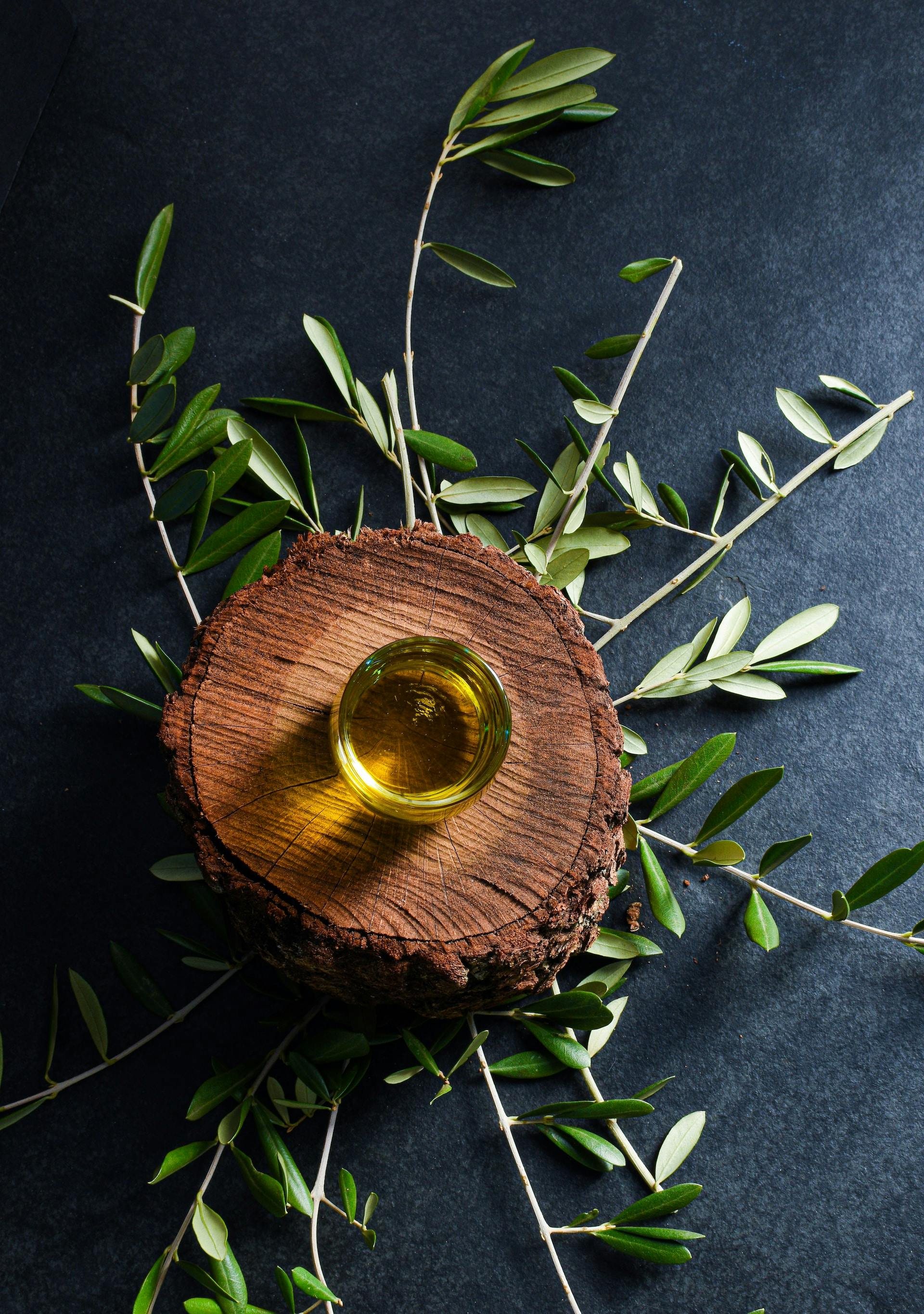 Glas mit öliger Flüssigkeit auf Holz mit Olivenblätter drum