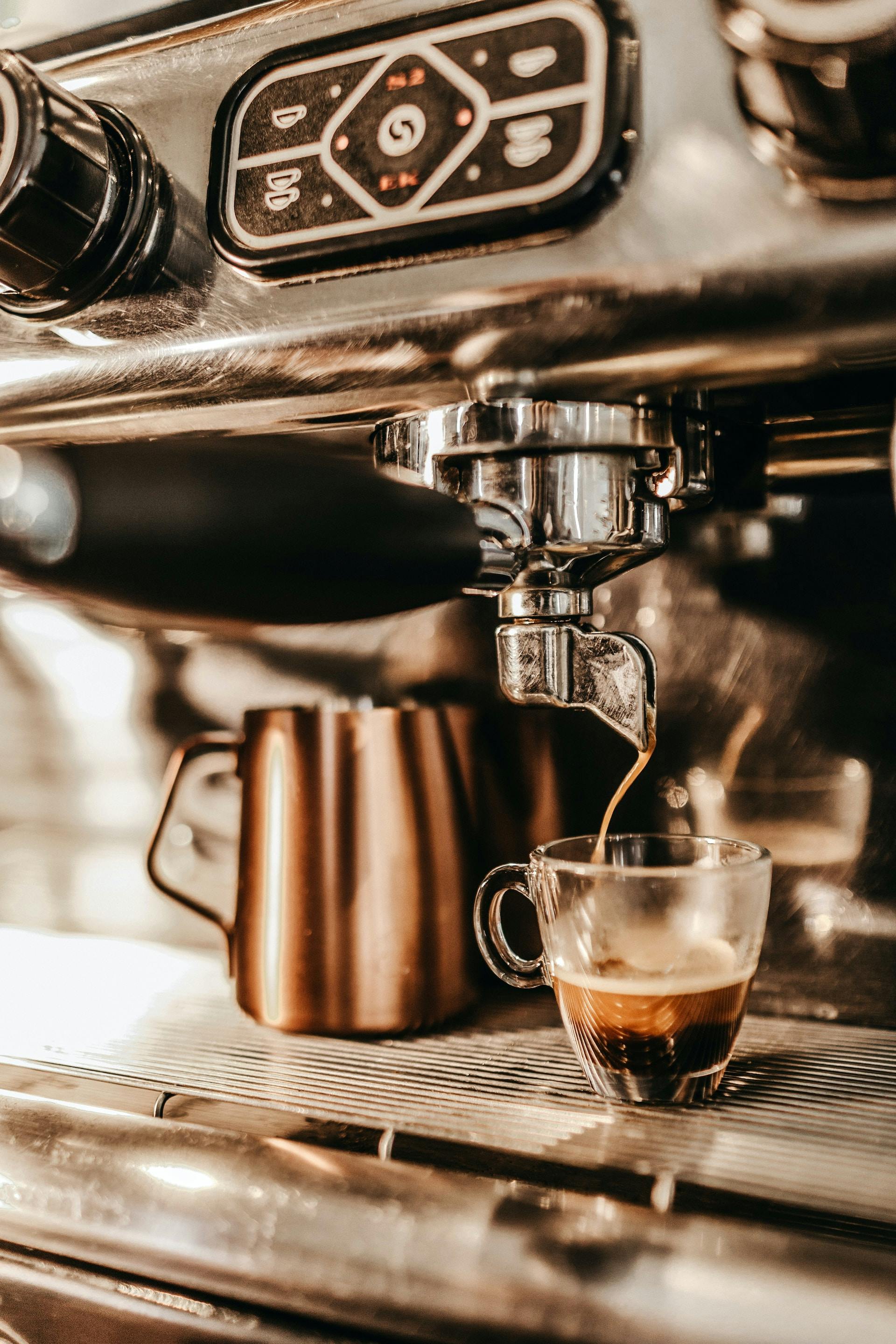 Kaffeemaschine füllt braune Flüssigkeit in Espressoglas 