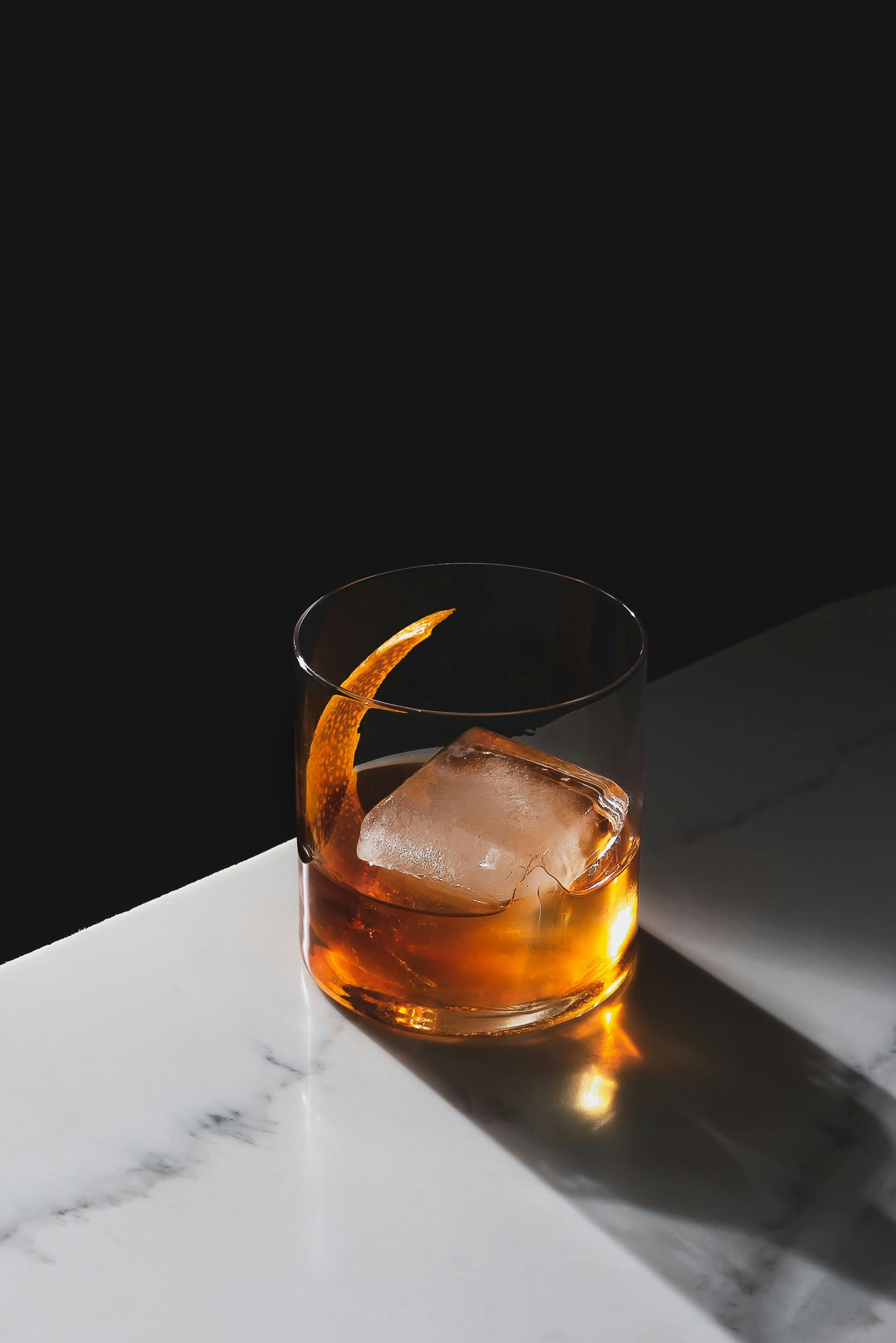 Ein Glas mit brauner Flüssigkeit und Eiswürfel steht auf einem Tisch 