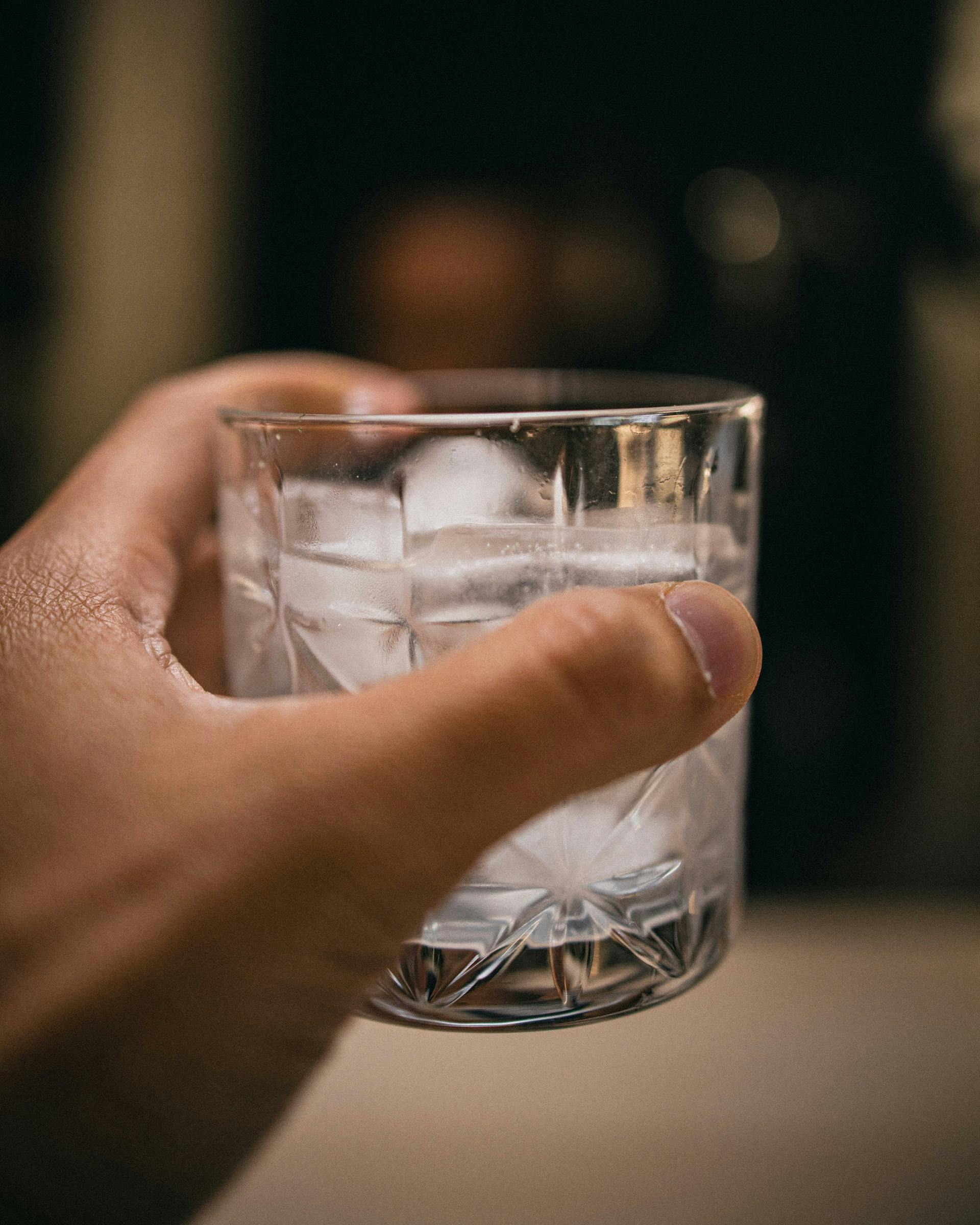 Glas mit klarer Flüssigkeit und Eis in einer Hand