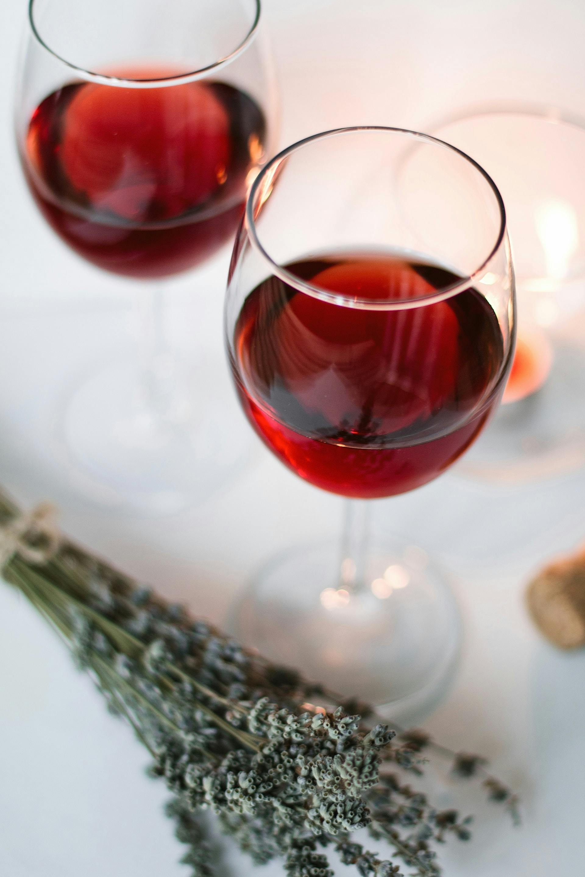 2 Weingläser auf weißer Tischdecke mit roter Flüssigkeit drinnen und Kräuter daneben