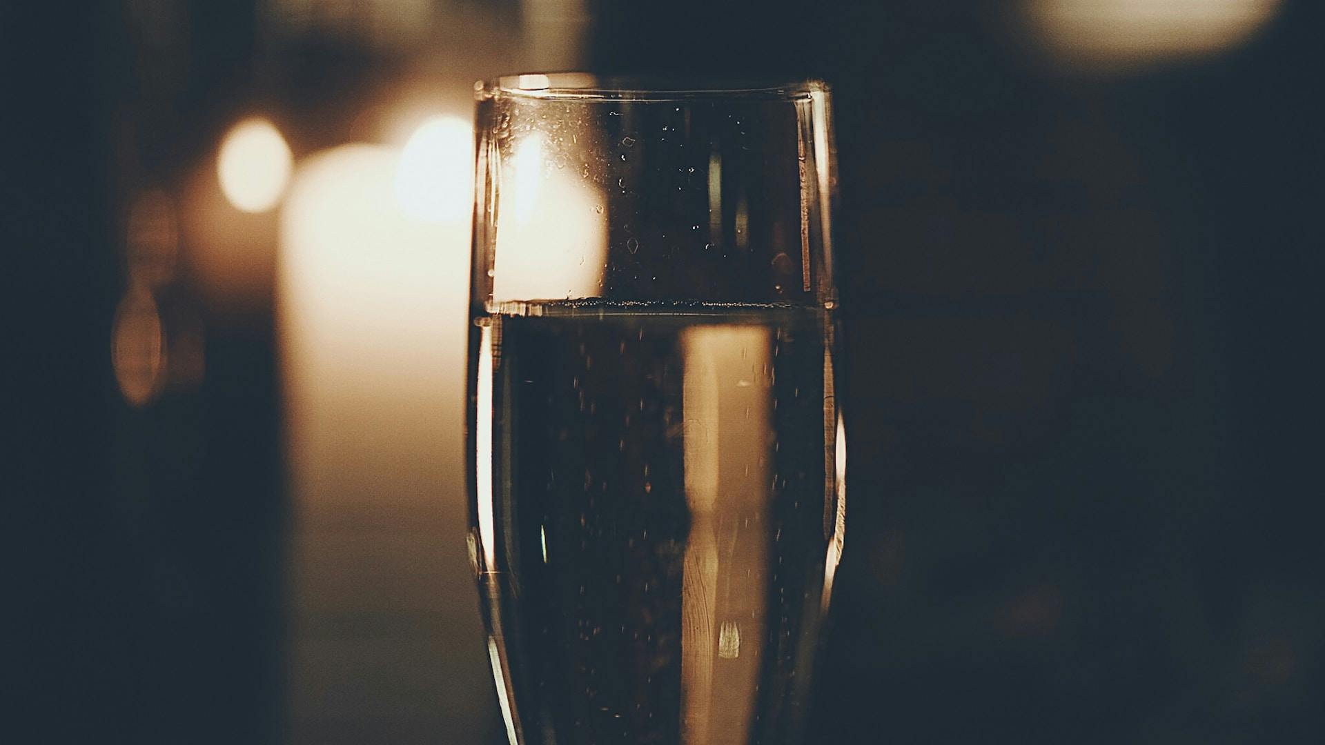 Dunkler Hintergrund wo Champagnerglas steht mit gelber Flüssigkeit drinnen