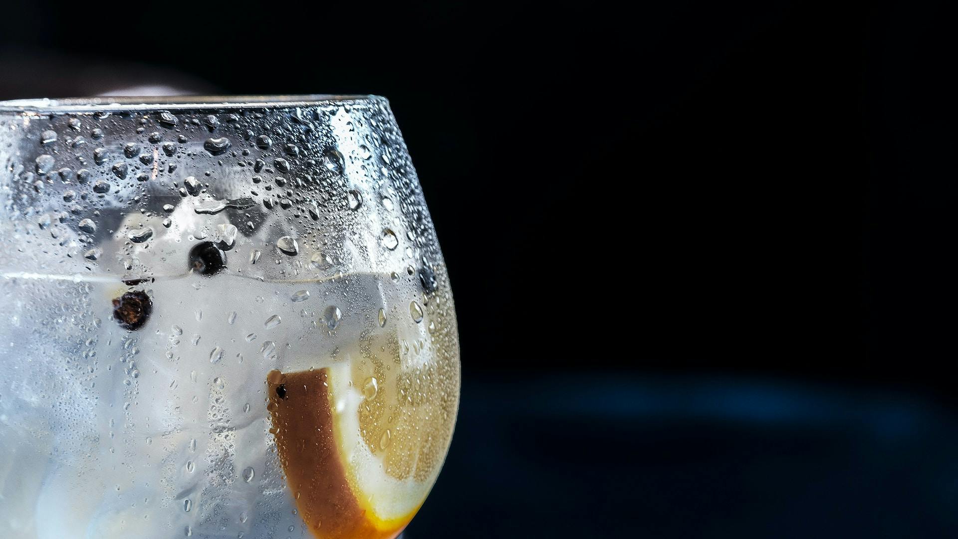 Rundes Glas mit klarer Flüssigkeit und Scheibe Zitrone auf dunklem Hintergrund