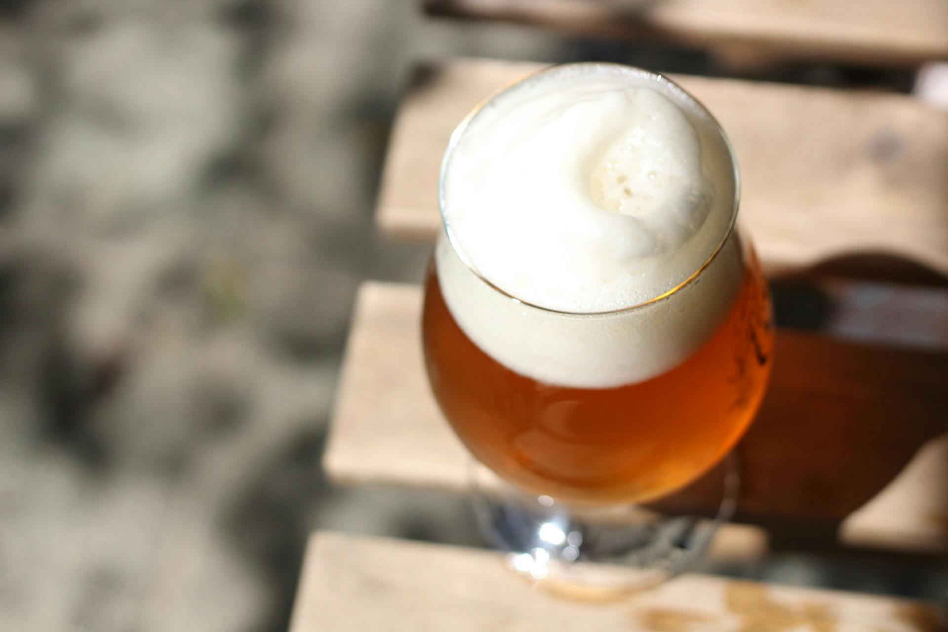 Klares Trinkglas mit Bier und Schaum auf einem Gartentisch.