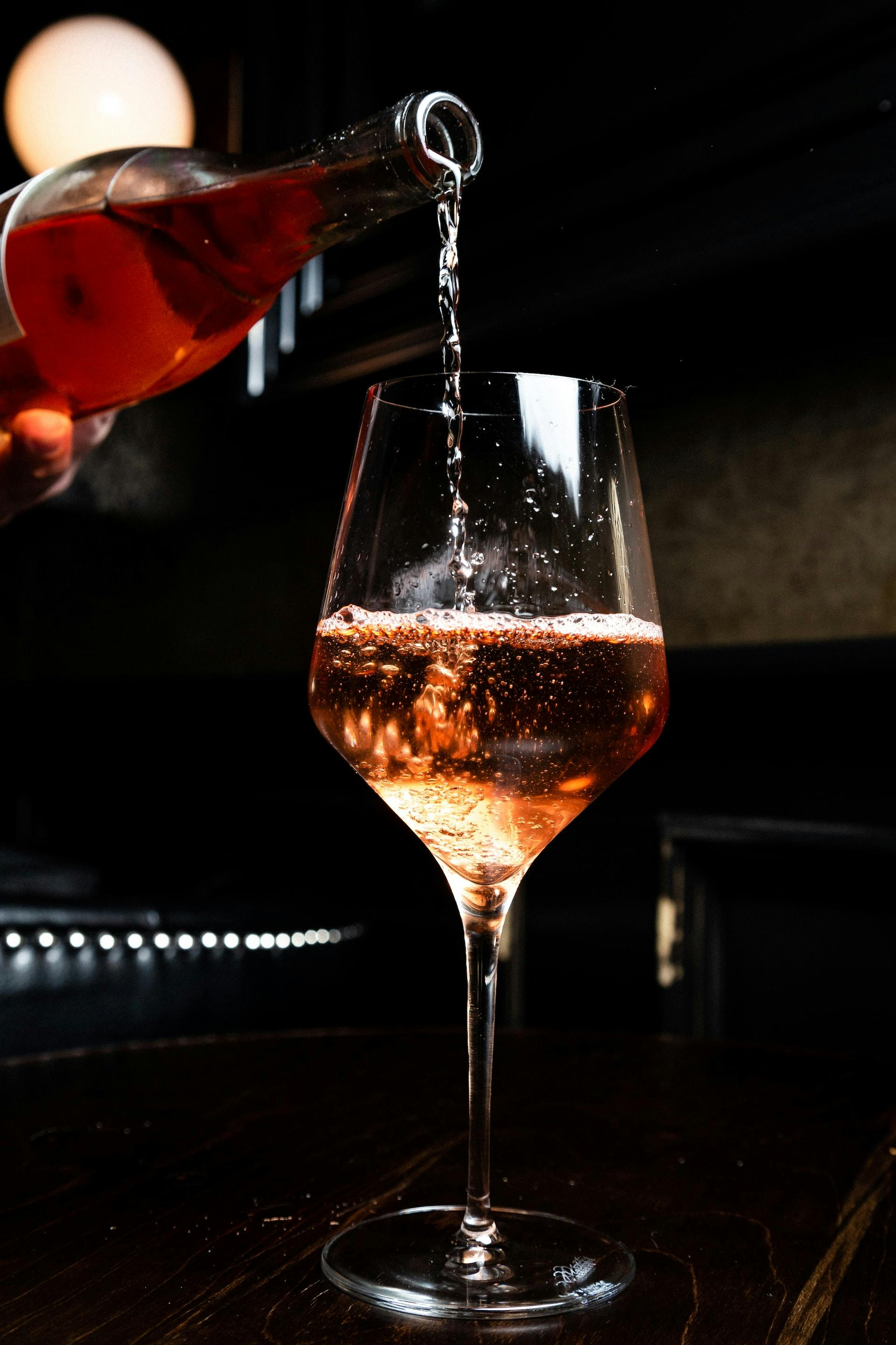 Flasche gießt rosafarbene Flüssigkeit ins Glas ein