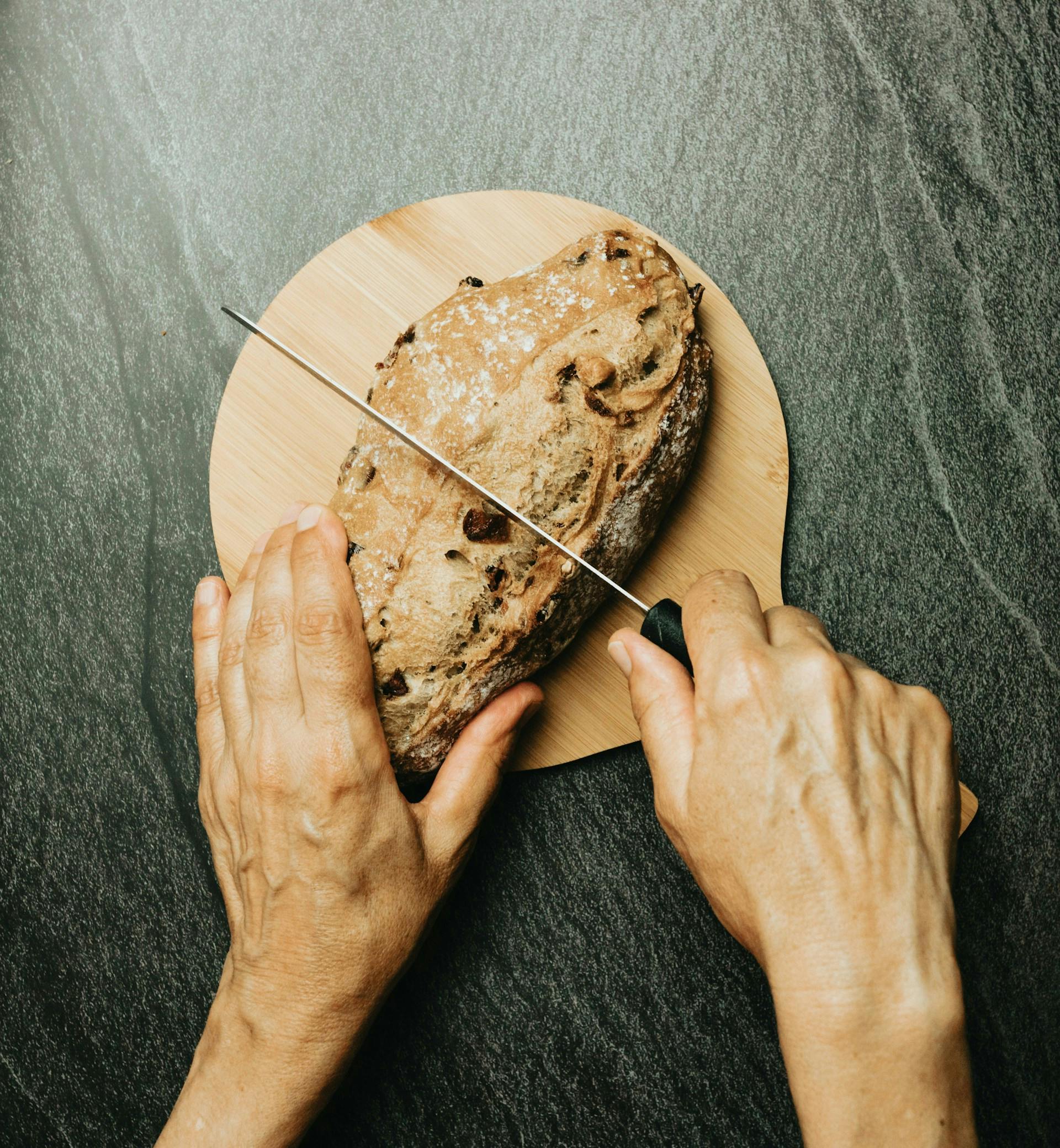 Auf einer dunklen Steinplatte wird Brot auf einem Holzbrett geschnitten