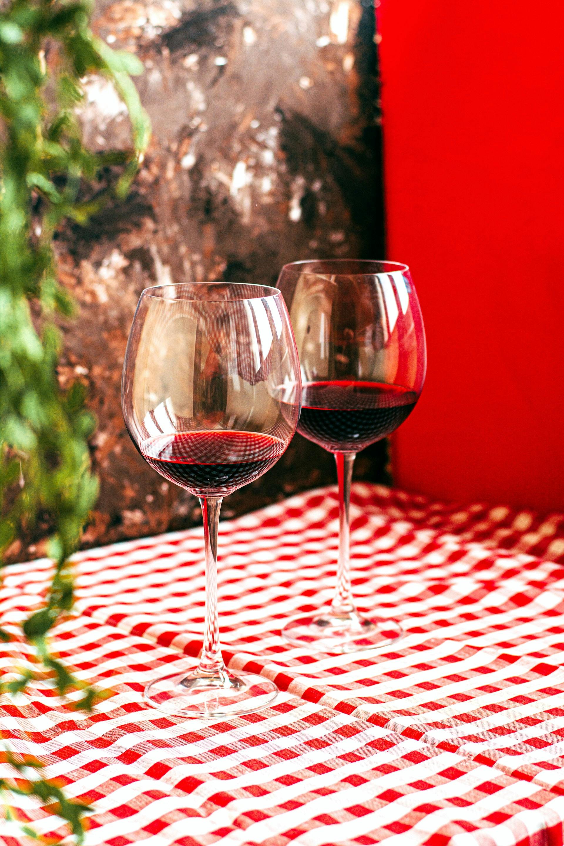 2 Weingläser mit roter Flüssigkeit auf rot weiß karierten Tischdecke