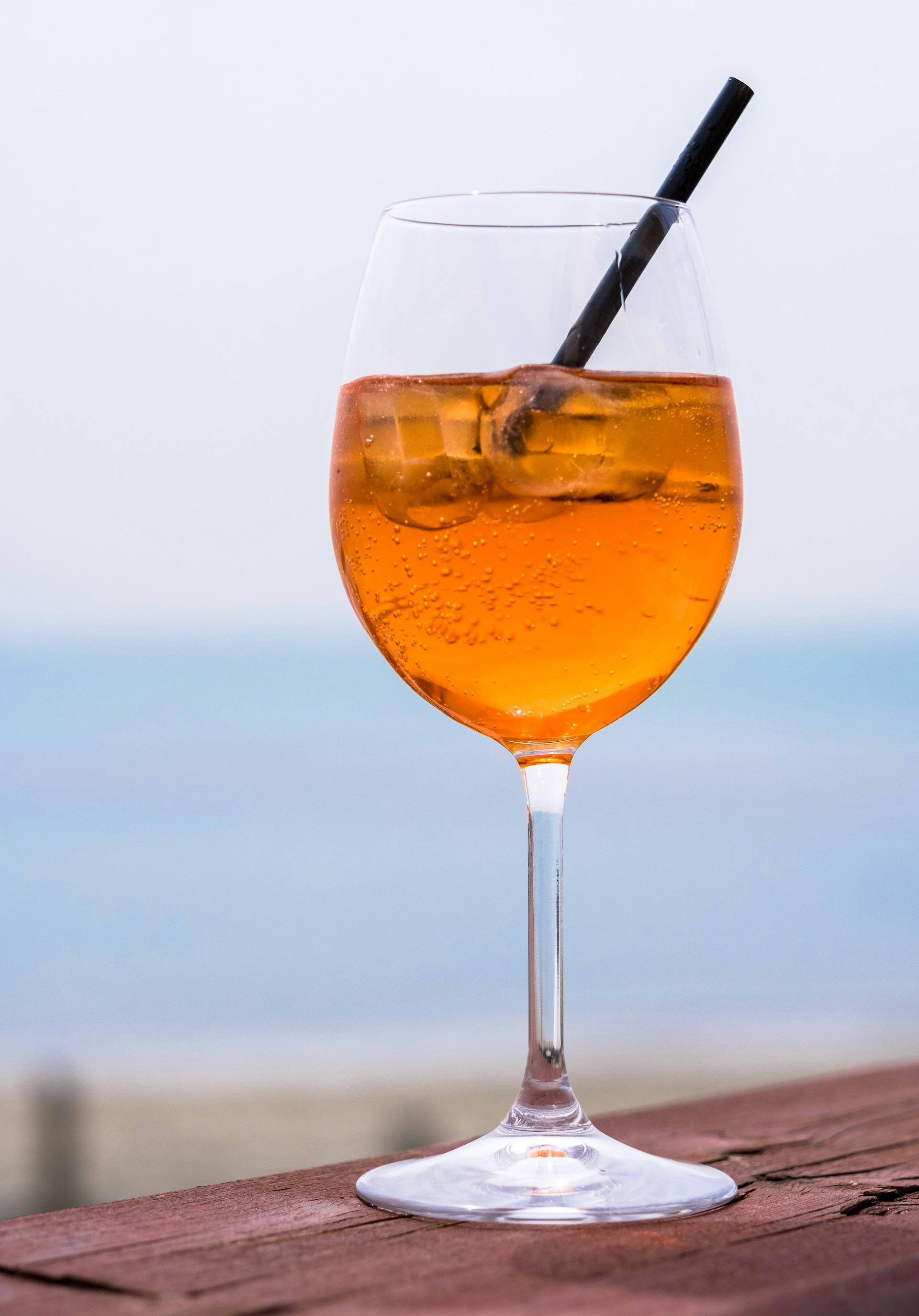 Weinglas mit orangefarbene Flüssigkeit und Strohhalm auf Holztisch
