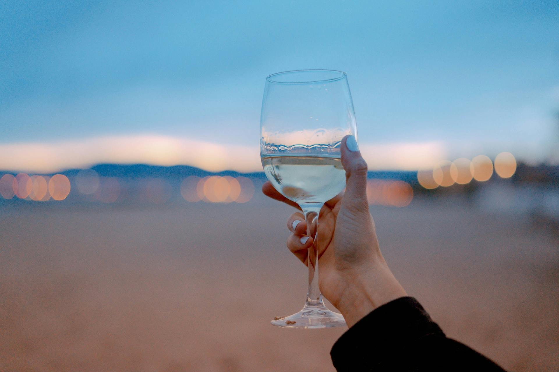 Hand hält Weinglas mit klarer Flüssigkeit vor verschwommenem Hintergrund